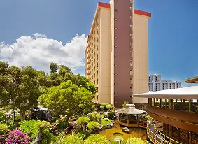 Mid-rise hotel tower surrounded by gardens and a pond