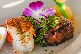 Steak and lobster tail garnished with herbs and an orchid