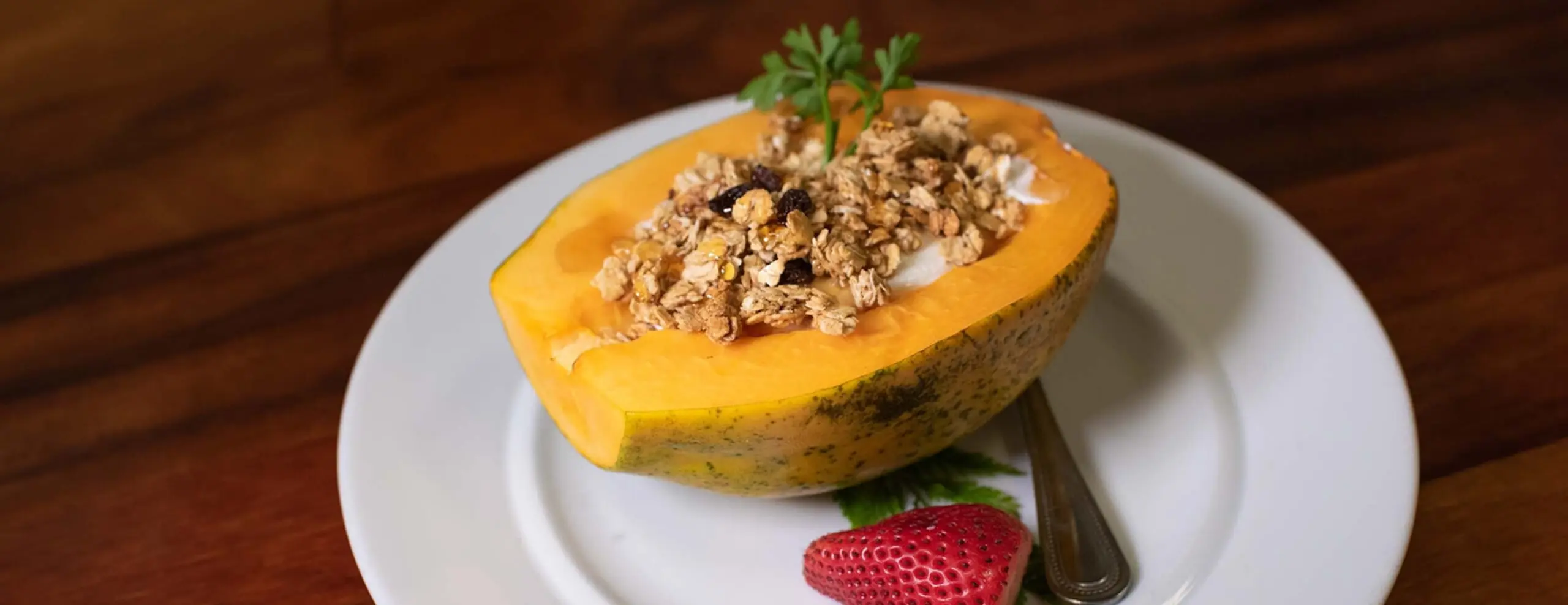 Half papaya filled with granola and yogurt on a white plate
