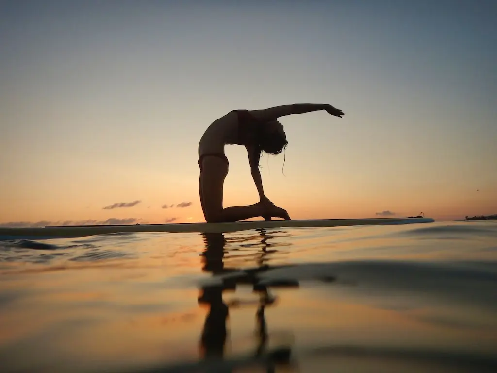 Person doing a backbend pose on a paddleboard at sunset