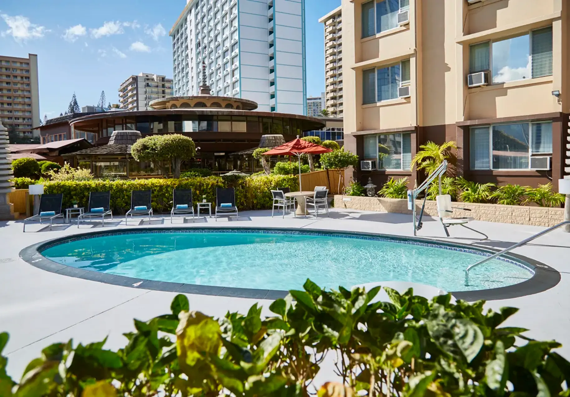 Outdoor pool area surrounded by lounge chairs and mid-rise buildings